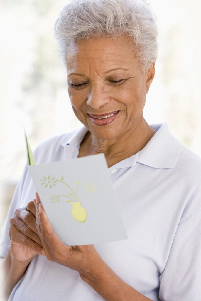 Elderly woman reading a greeting card with a smile.