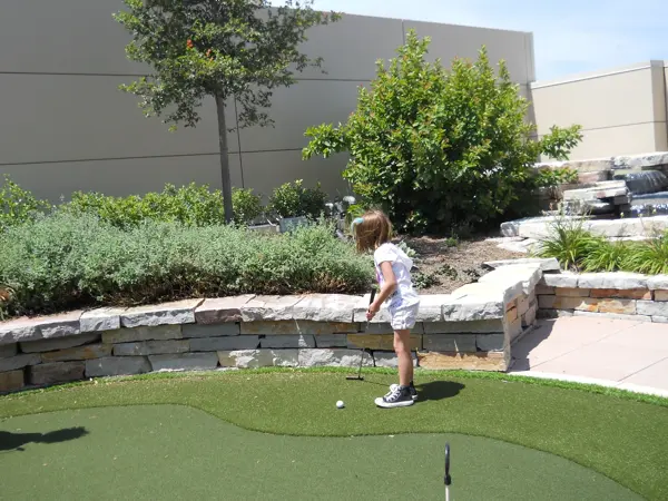 A young child playing mini-golf outdoors on a sunny day.