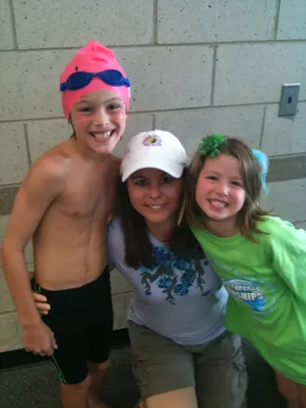 Three smiling children posing together indoors, one wearing swim gear.