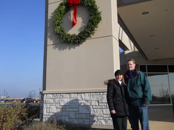 Two people standing outside a building decorated with a large holiday wreath.