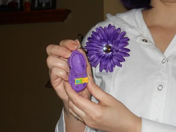Person holding a purple digital device with a large purple flower pinned on their shirt.
