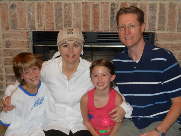 A smiling family of four posing indoors against a brick wall.