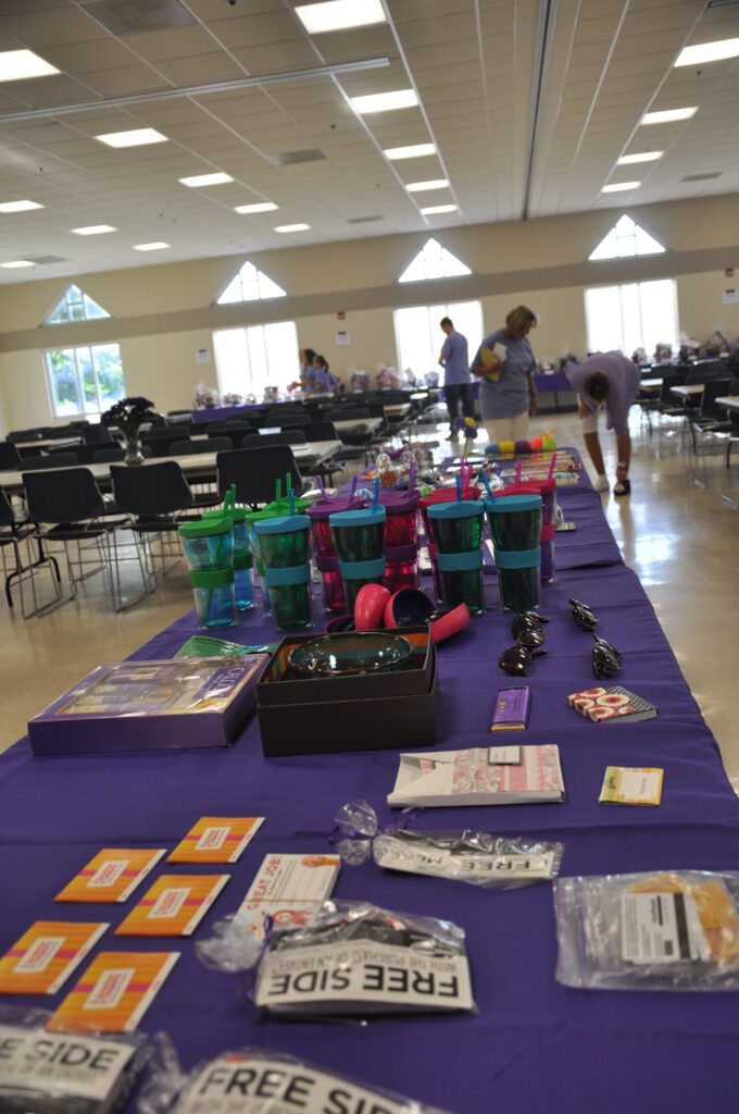 Table with craft supplies and paint bottles in a community hall.