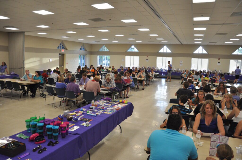 Community gathering with people seated at tables in a large hall.