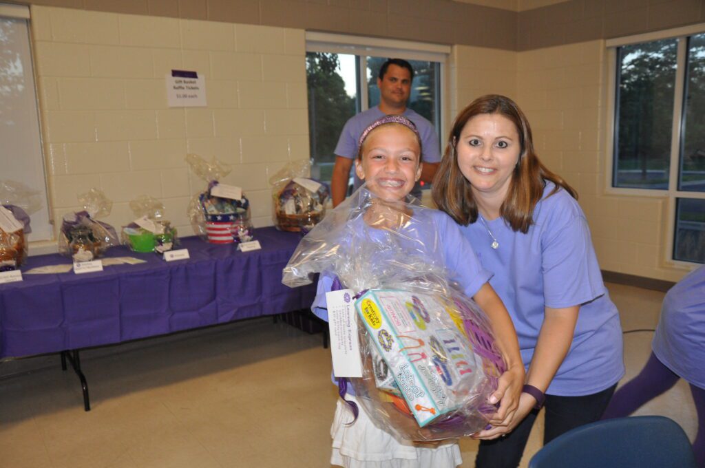 Two women smiling, one holding a gift basket wrapped in cellophane.
