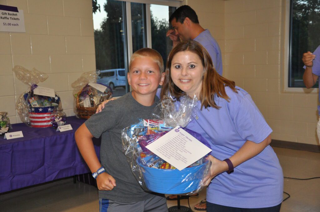 Two people smiling and holding a gift basket indoors.