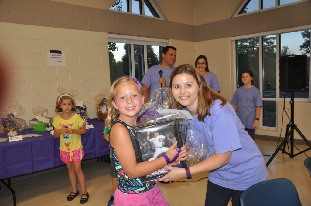 Two girls smiling and holding a trophy together indoors.