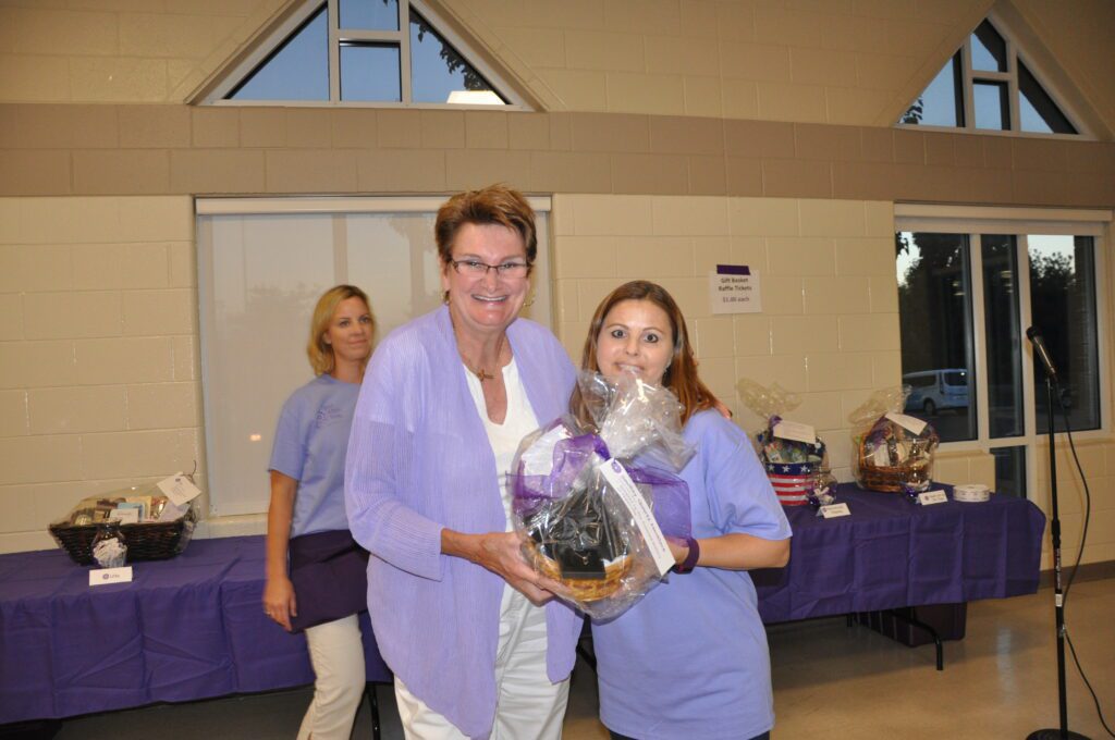 Two women smiling and holding a gift basket indoors.