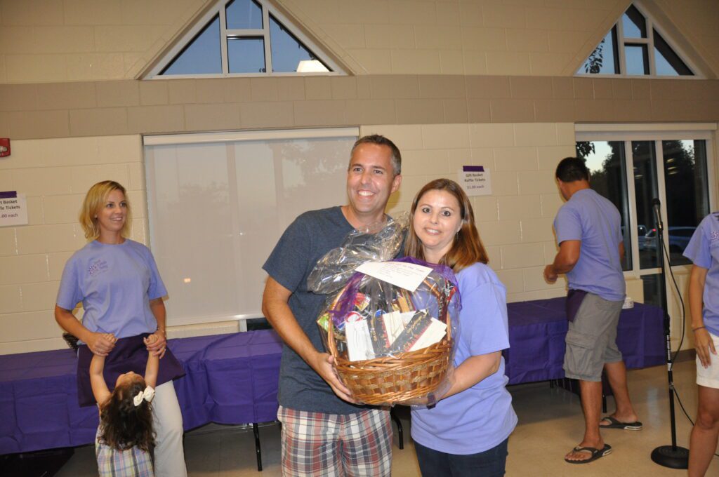 A man and woman holding a gift basket, smiling at an indoor event.