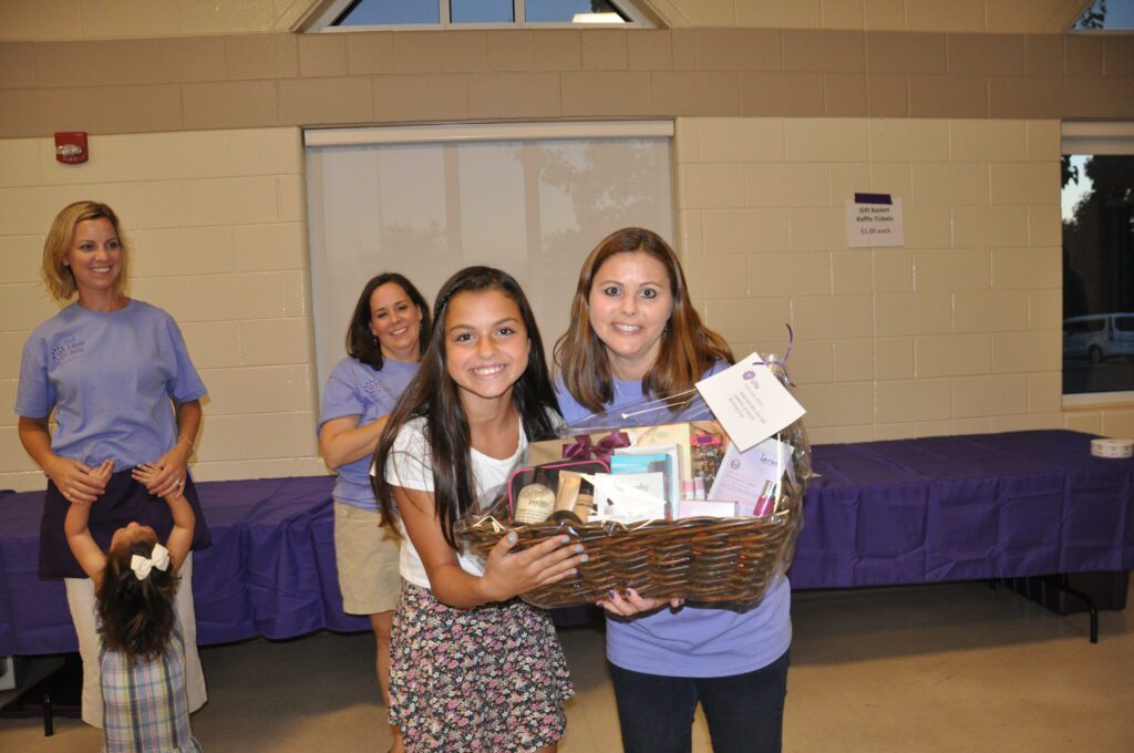 Two young women smiling, holding a basket filled with various items indoors.