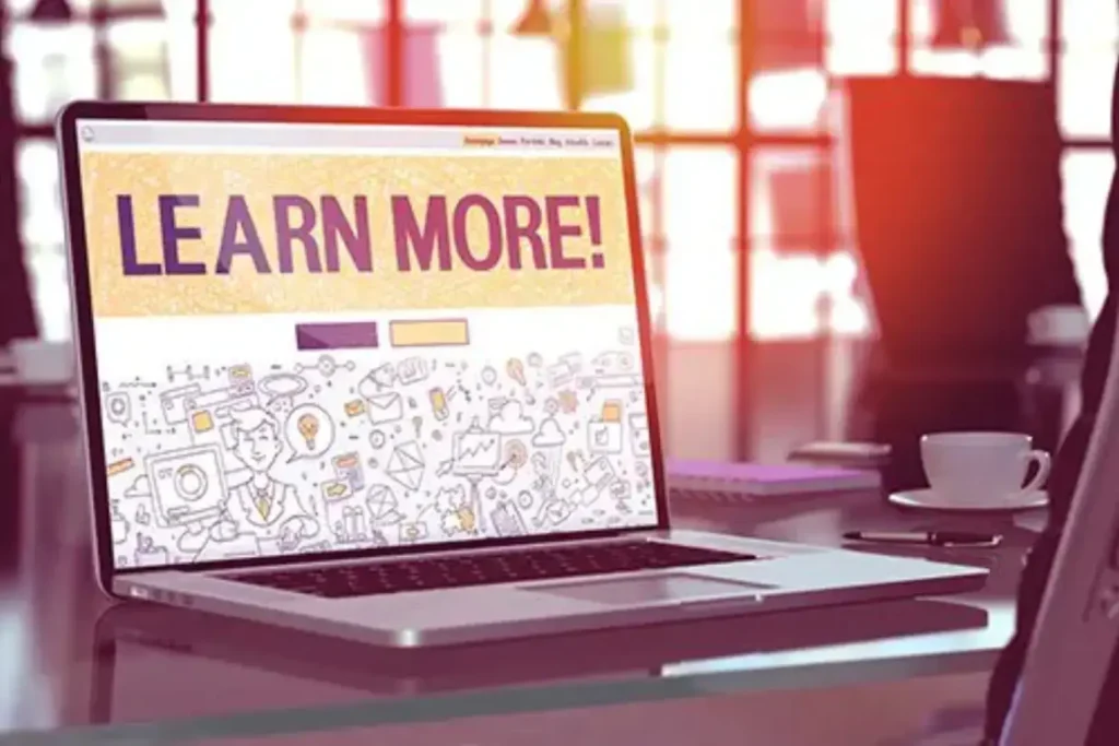 Laptop screen showing 'LEARN MORE!' on a desk in a bright office.